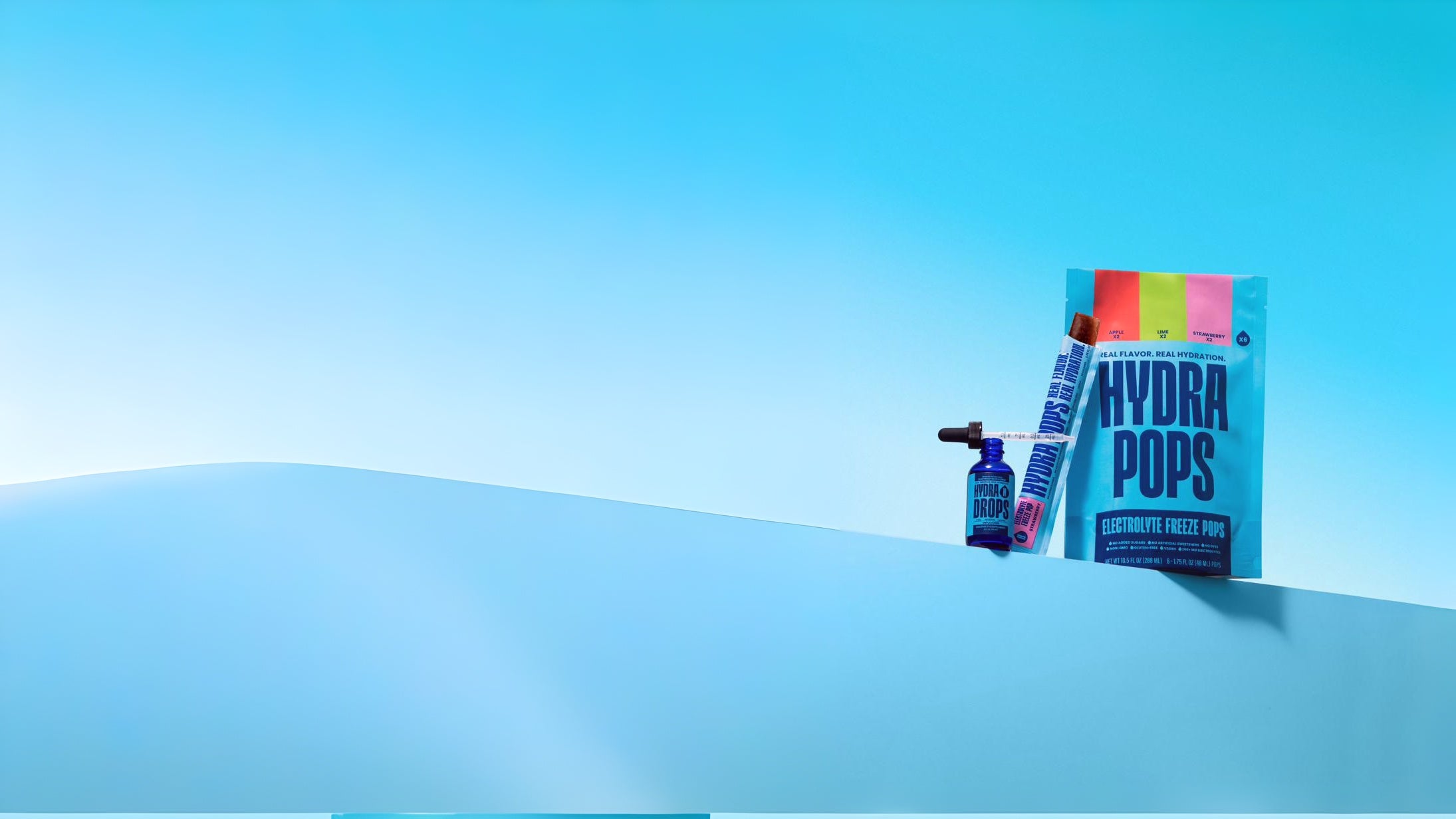Hydra Drops dropper bottle beside a Hydra Pops freeze pop and Hydra Pops variety bag on a cyan background